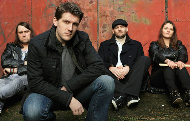 A bunch of rockers, hanging out in front of a rusty metal wall. From left to right: Billy Dedman, Paul Muir, Paul Turley, Donna Peters